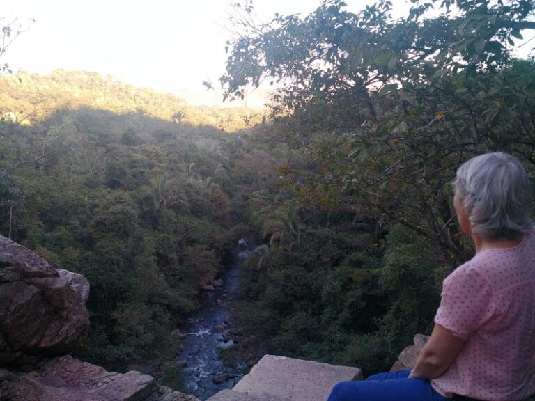Mulher observa o vale e o córrego da RPPN Cachoeira do Tombador cercados por mata nativa