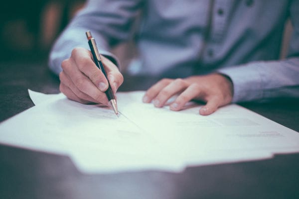 Mão preenchendo documentos de licenciamento com caneta sobre a mesa